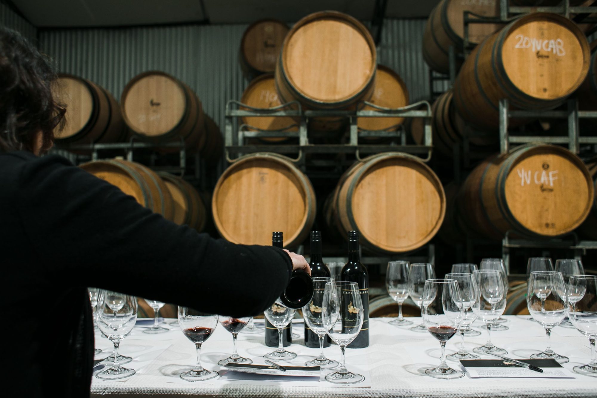 Weinprobe im Weinkeller: Wein wird vor Fässern in Gläser eingeschenkt